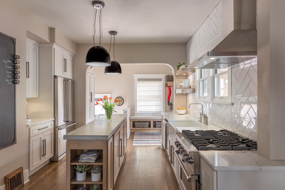 This is an example of a traditional galley kitchen/diner in Denver with a belfast sink, shaker cabinets, white cabinets, concrete worktops, white splashback, metro tiled splashback, stainless steel appliances, medium hardwood flooring, an island and brown floors.