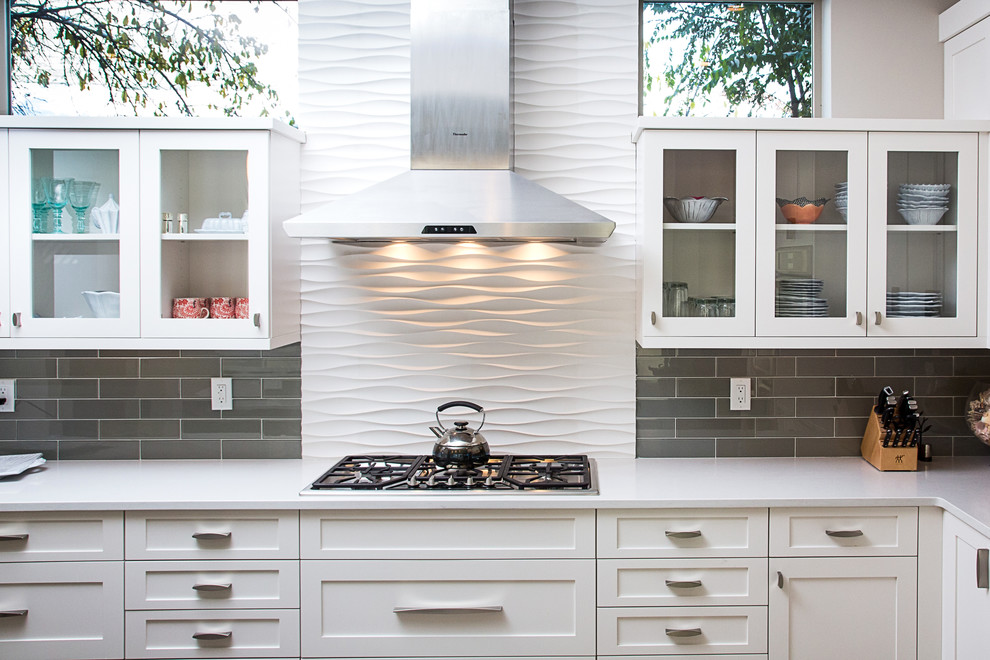 Bild på ett mellanstort funkis kök, med vita skåp, bänkskiva i kvarts, grått stänkskydd, stänkskydd i glaskakel, rostfria vitvaror, en undermonterad diskho, luckor med infälld panel och en köksö