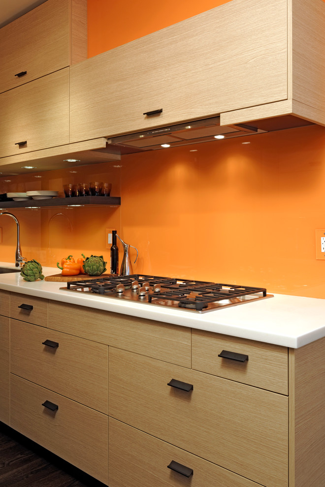 Modern inredning av ett litet kök, med en undermonterad diskho, släta luckor, skåp i ljust trä, bänkskiva i kvartsit, orange stänkskydd, rostfria vitvaror, mörkt trägolv och glaspanel som stänkskydd