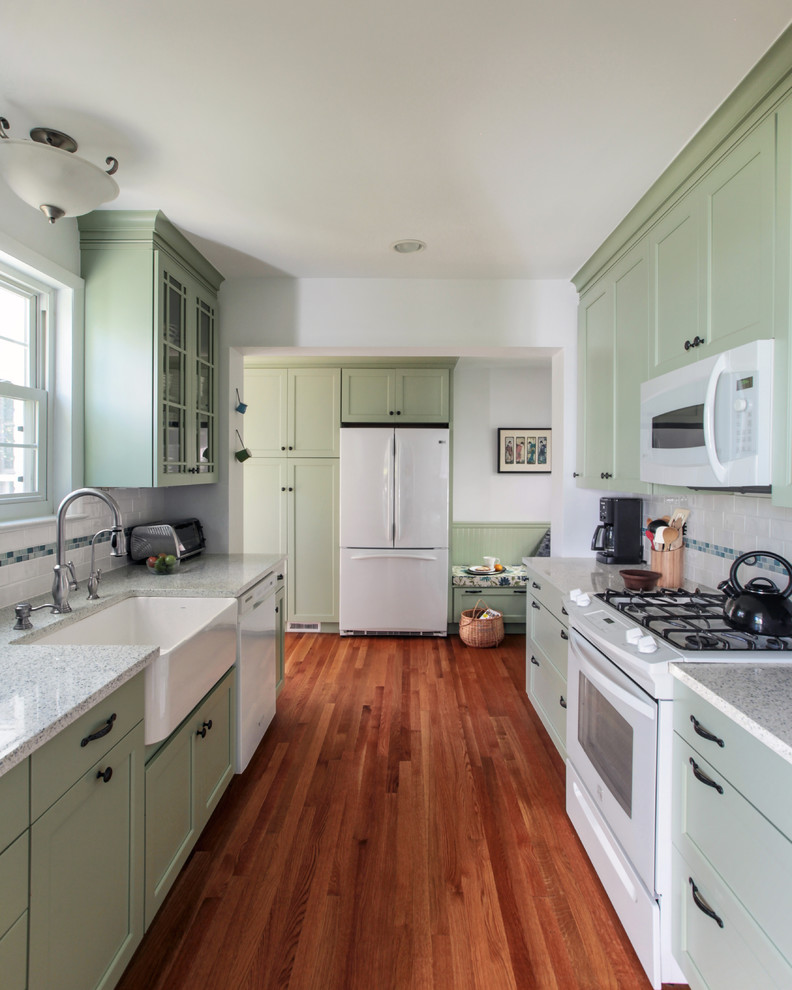 Exempel på ett avskilt, litet klassiskt u-kök, med en rustik diskho, luckor med infälld panel, gröna skåp, bänkskiva i kvarts, vitt stänkskydd, stänkskydd i keramik, vita vitvaror och mellanmörkt trägolv