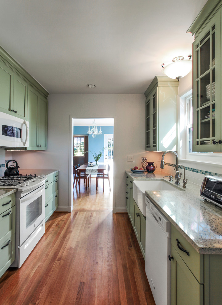 Example of a small classic galley medium tone wood floor enclosed kitchen design in DC Metro with a farmhouse sink, raised-panel cabinets, green cabinets, quartz countertops, white backsplash, ceramic backsplash, white appliances and no island