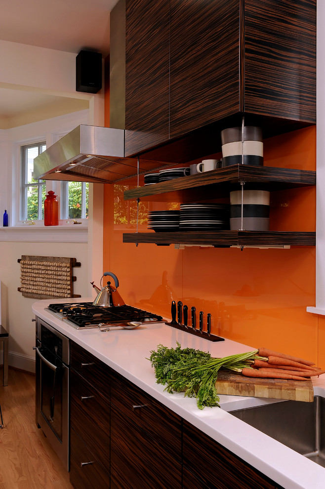 Idéer för ett mellanstort modernt kök, med släta luckor, skåp i mörkt trä, bänkskiva i kvartsit, orange stänkskydd, stänkskydd i glaskakel, rostfria vitvaror, en köksö, en undermonterad diskho och ljust trägolv