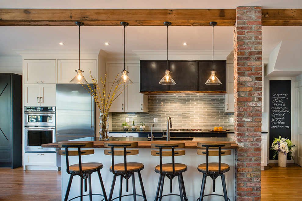 Diseño de cocina comedor lineal industrial de tamaño medio con fregadero bajoencimera, armarios con rebordes decorativos, puertas de armario blancas, encimera de granito, salpicadero gris, salpicadero con mosaicos de azulejos, electrodomésticos de acero inoxidable, suelo de madera en tonos medios, una isla, suelo beige y encimeras negras