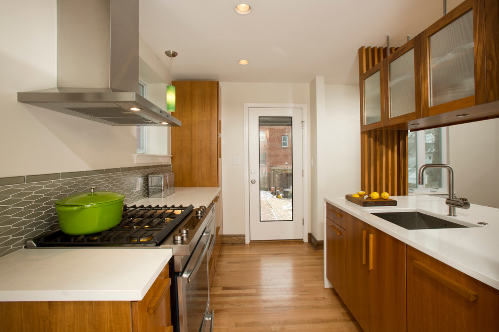 Bild på ett mellanstort eklektiskt kök, med en undermonterad diskho, släta luckor, skåp i mellenmörkt trä, bänkskiva i kvarts, grönt stänkskydd, stänkskydd i glaskakel, rostfria vitvaror och mellanmörkt trägolv