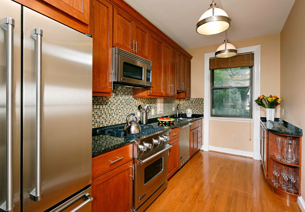 Modelo de cocina lineal contemporánea cerrada con salpicadero con mosaicos de azulejos, electrodomésticos de acero inoxidable, salpicadero gris, armarios con paneles empotrados y puertas de armario de madera oscura