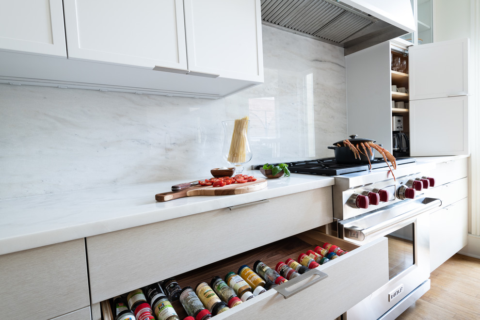 Design ideas for a medium sized retro single-wall kitchen pantry in DC Metro with a submerged sink, shaker cabinets, white cabinets, marble worktops, white splashback, marble splashback, stainless steel appliances, light hardwood flooring, an island, brown floors and white worktops.