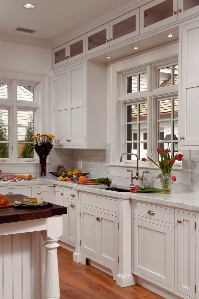 Eat-in kitchen - large traditional u-shaped light wood floor and beige floor eat-in kitchen idea in DC Metro with an undermount sink, recessed-panel cabinets, white cabinets, marble countertops, beige backsplash, stone tile backsplash, stainless steel appliances and an island