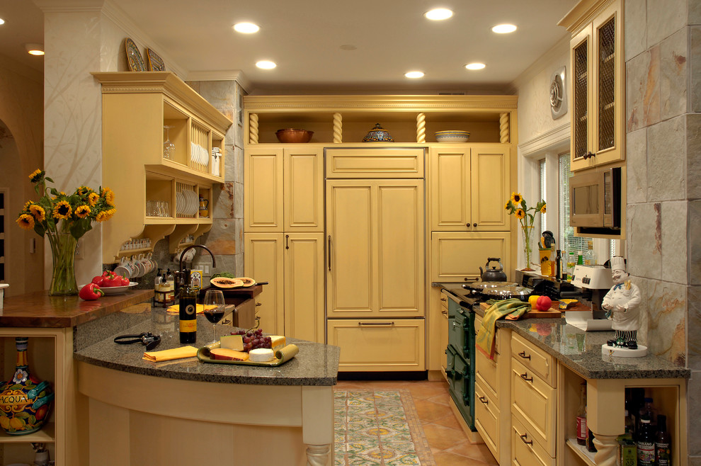 Design ideas for a medium sized classic u-shaped kitchen pantry in DC Metro with a belfast sink, beaded cabinets, yellow cabinets, granite worktops, grey splashback, stone tiled splashback, integrated appliances, terracotta flooring, a breakfast bar and beige floors.