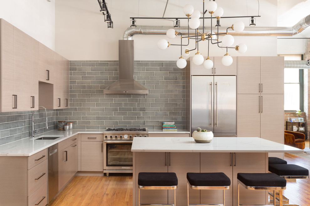Example of a trendy l-shaped medium tone wood floor and brown floor open concept kitchen design in Chicago with an undermount sink, flat-panel cabinets, light wood cabinets, gray backsplash, subway tile backsplash, stainless steel appliances and an island