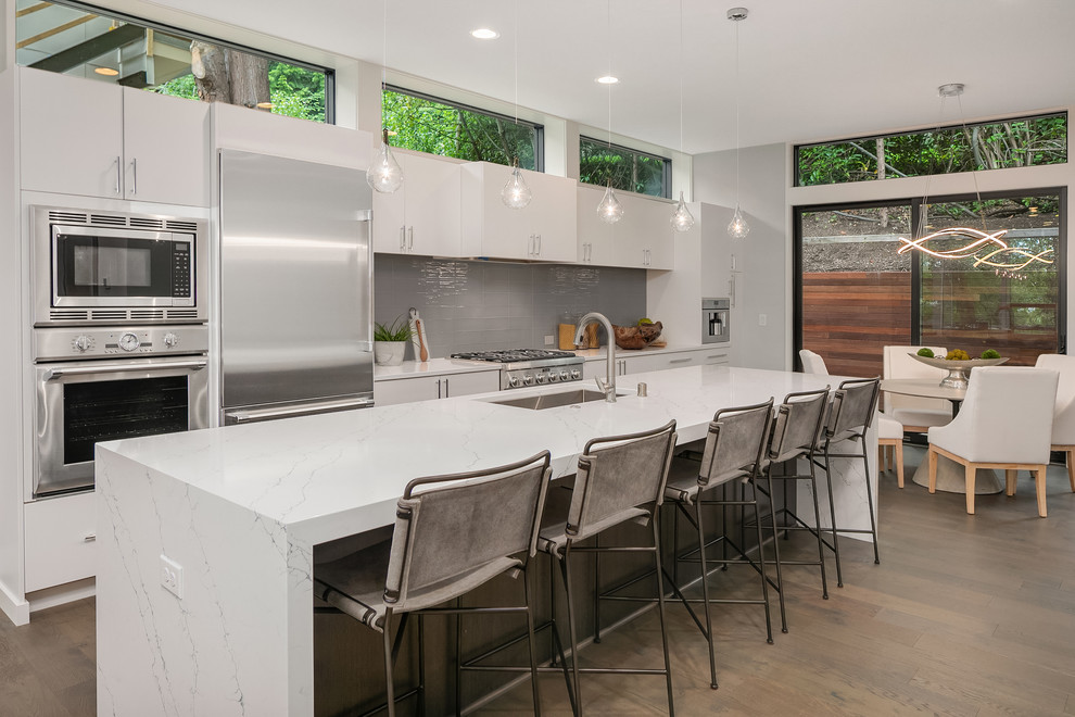 Open concept kitchen - contemporary galley dark wood floor and brown floor open concept kitchen idea in Seattle with an undermount sink, flat-panel cabinets, white cabinets, gray backsplash, stainless steel appliances, an island and white countertops
