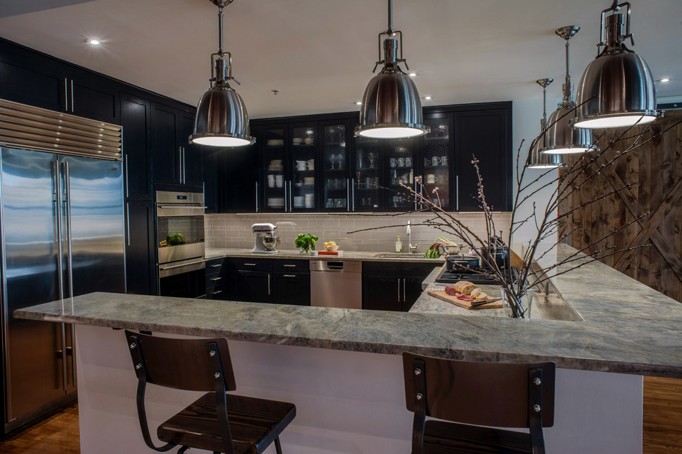 This is an example of a medium sized industrial u-shaped kitchen in Philadelphia with shaker cabinets, black cabinets, grey splashback, glass tiled splashback and stainless steel appliances.