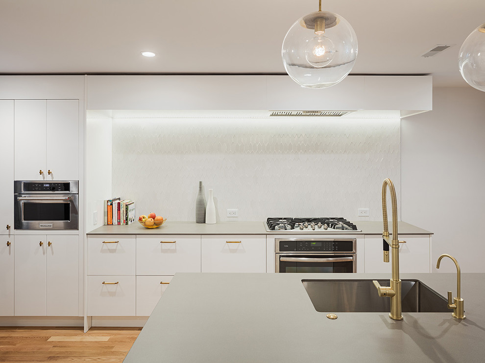 Trendy medium tone wood floor kitchen photo in Philadelphia with an undermount sink, flat-panel cabinets, white cabinets, white backsplash, stainless steel appliances and an island