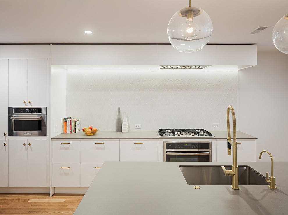 Moderne Küche mit Unterbauwaschbecken, flächenbündigen Schrankfronten, weißen Schränken, Küchenrückwand in Weiß, Küchengeräten aus Edelstahl, braunem Holzboden und Kücheninsel in Philadelphia