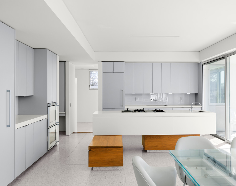 На фото: параллельная кухня в стиле модернизм с столешницей из акрилового камня, плоскими фасадами, серыми фасадами, серым фартуком, техникой под мебельный фасад и обеденным столом