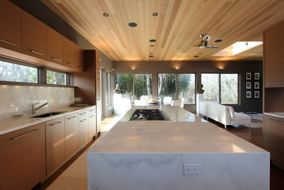 Example of a mid-sized trendy single-wall medium tone wood floor open concept kitchen design in New York with a drop-in sink, flat-panel cabinets, medium tone wood cabinets, marble countertops, white backsplash, stone slab backsplash, paneled appliances and an island