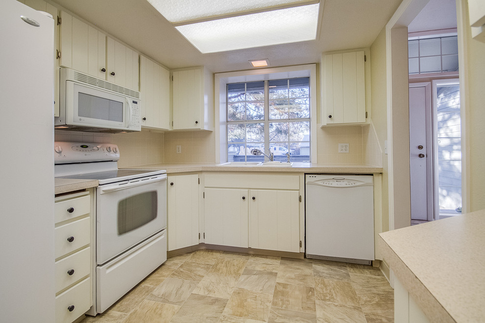 Photo of a small enclosed kitchen in Boise with a double-bowl sink, beaded cabinets, white cabinets, laminate countertops, beige splashback, porcelain splashback, white appliances and lino flooring.