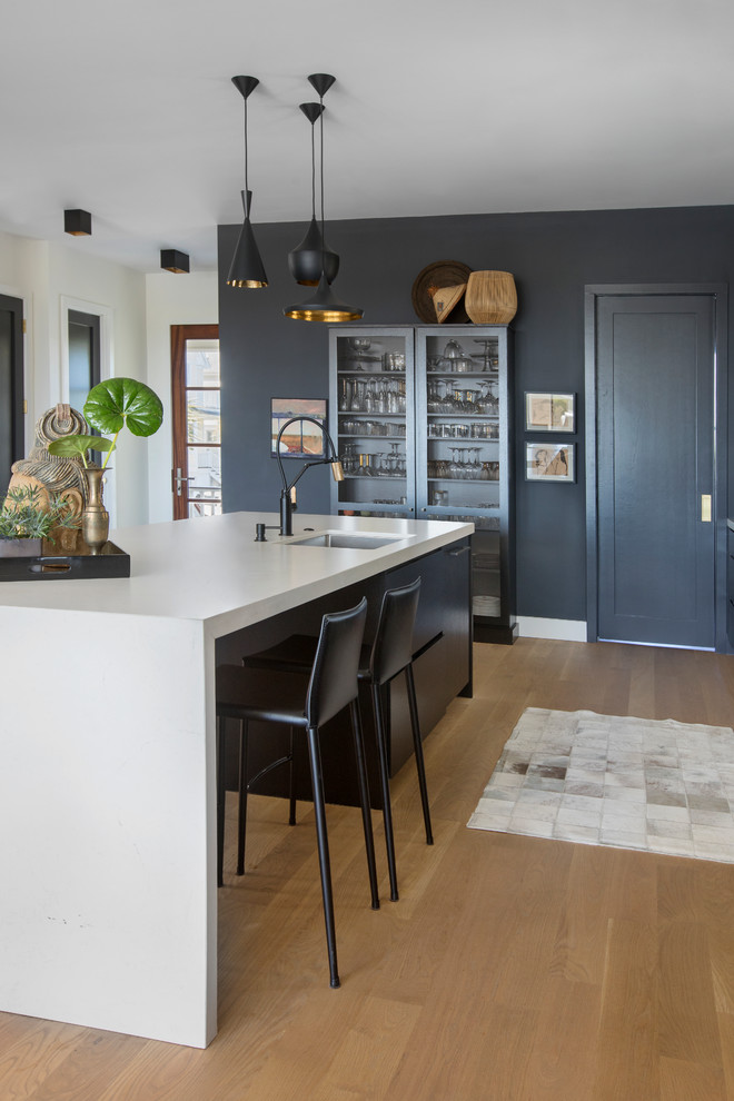 Foto de cocina actual con fregadero bajoencimera, puertas de armario negras, suelo de madera clara, una isla, encimeras blancas y armarios con paneles lisos
