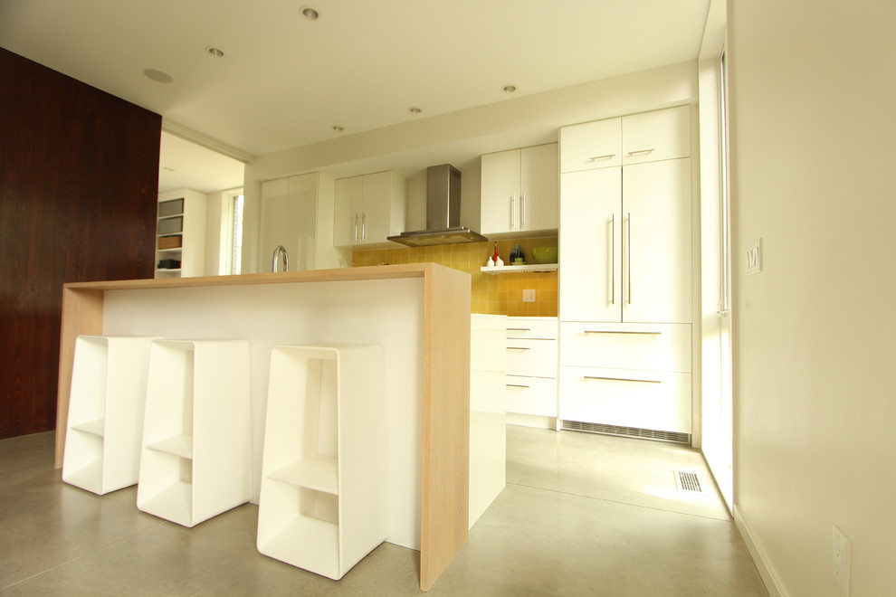Bild på ett litet funkis linjärt kök med öppen planlösning, med en dubbel diskho, släta luckor, vita skåp, bänkskiva i kvarts, gult stänkskydd, stänkskydd i keramik, integrerade vitvaror, betonggolv och en köksö
