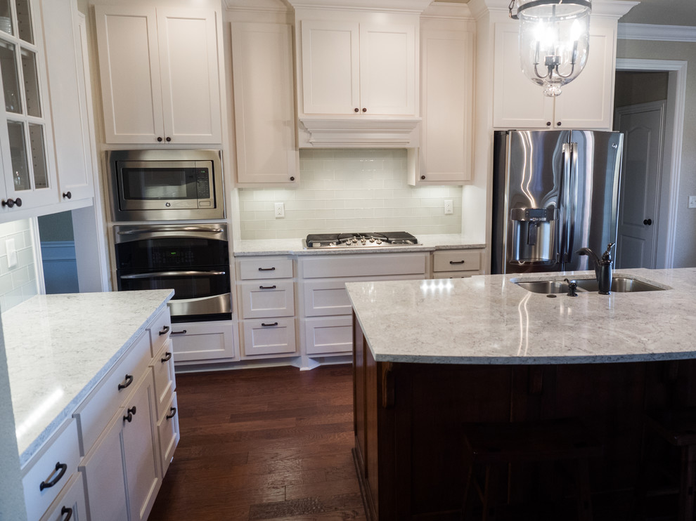 Inspiration for a mid-sized transitional l-shaped dark wood floor open concept kitchen remodel in Other with a double-bowl sink, shaker cabinets, white cabinets, quartz countertops, white backsplash, glass tile backsplash, stainless steel appliances and an island
