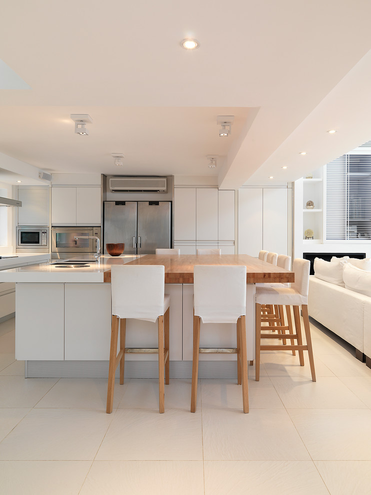 Idéer för ett modernt vit kök, med släta luckor, vita skåp, rostfria vitvaror, en köksö och beiget golv