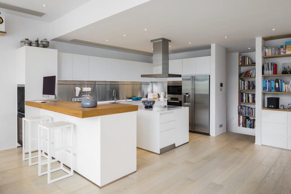 Photo of a modern u-shaped kitchen in Hong Kong with flat-panel cabinets, white cabinets, metallic splashback, stainless steel appliances, light hardwood flooring, an island, beige floors and white worktops.