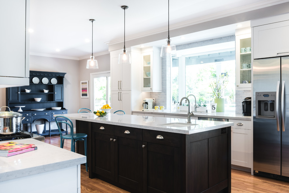 Example of a mid-sized trendy l-shaped medium tone wood floor and brown floor open concept kitchen design in San Francisco with an undermount sink, shaker cabinets, white cabinets, quartzite countertops, white backsplash, marble backsplash, stainless steel appliances and an island