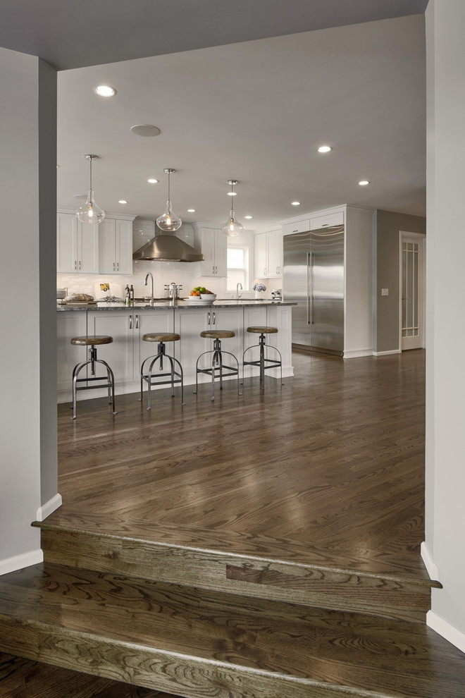Eat-in kitchen - large craftsman l-shaped dark wood floor and brown floor eat-in kitchen idea in Seattle with a drop-in sink, shaker cabinets, white cabinets, white backsplash, ceramic backsplash, stainless steel appliances, an island, quartz countertops and gray countertops
