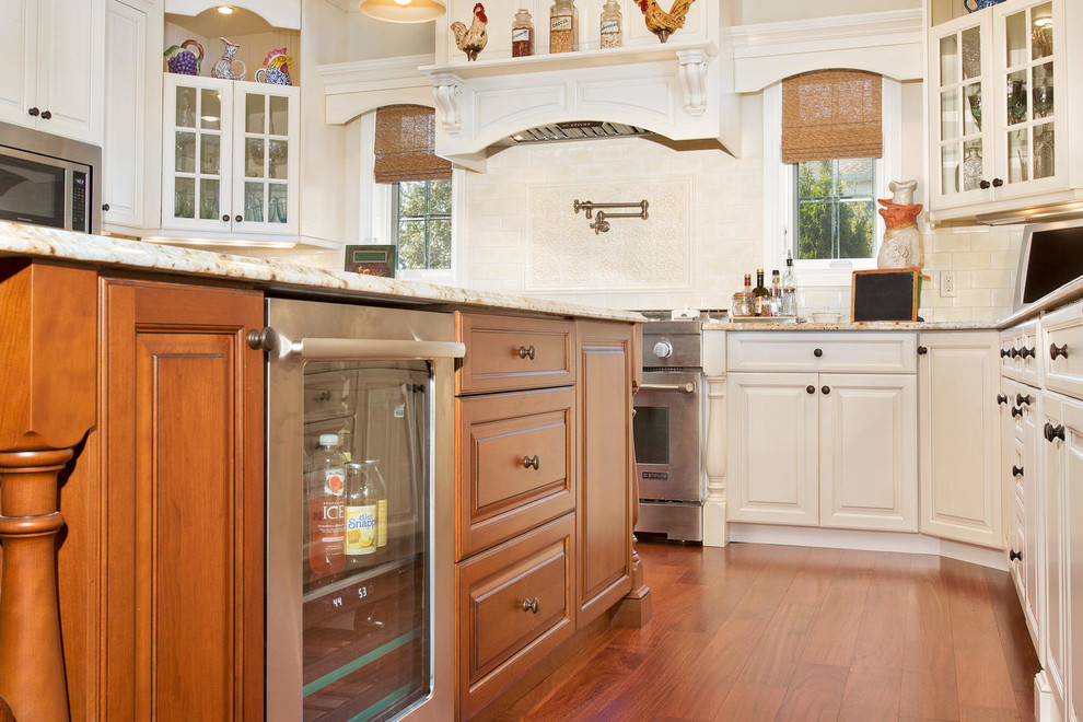 Klassisk inredning av ett stort kök, med en undermonterad diskho, luckor med upphöjd panel, vita skåp, granitbänkskiva, vitt stänkskydd, stänkskydd i keramik, rostfria vitvaror, mellanmörkt trägolv och en köksö