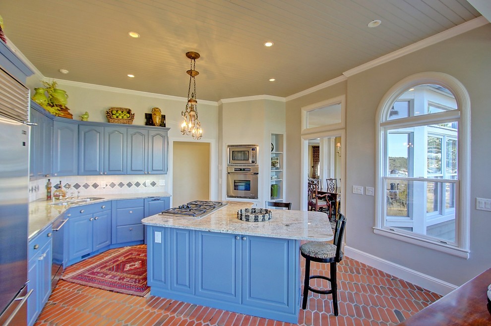 Maritim inredning av ett kök och matrum, med en dubbel diskho, blå skåp, granitbänkskiva, flerfärgad stänkskydd, stänkskydd i keramik, rostfria vitvaror, klinkergolv i terrakotta och en köksö