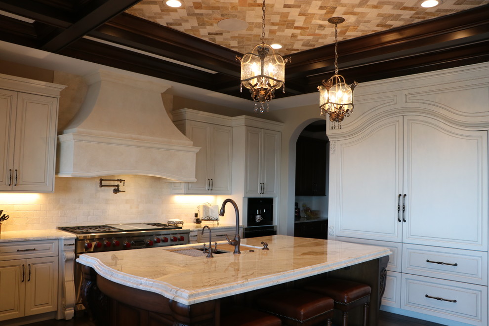 Idéer för att renovera ett stort medelhavsstil beige beige u-kök, med en undermonterad diskho, luckor med upphöjd panel, vita skåp, granitbänkskiva, vitt stänkskydd, stänkskydd i stenkakel, rostfria vitvaror, mörkt trägolv, en köksö och brunt golv
