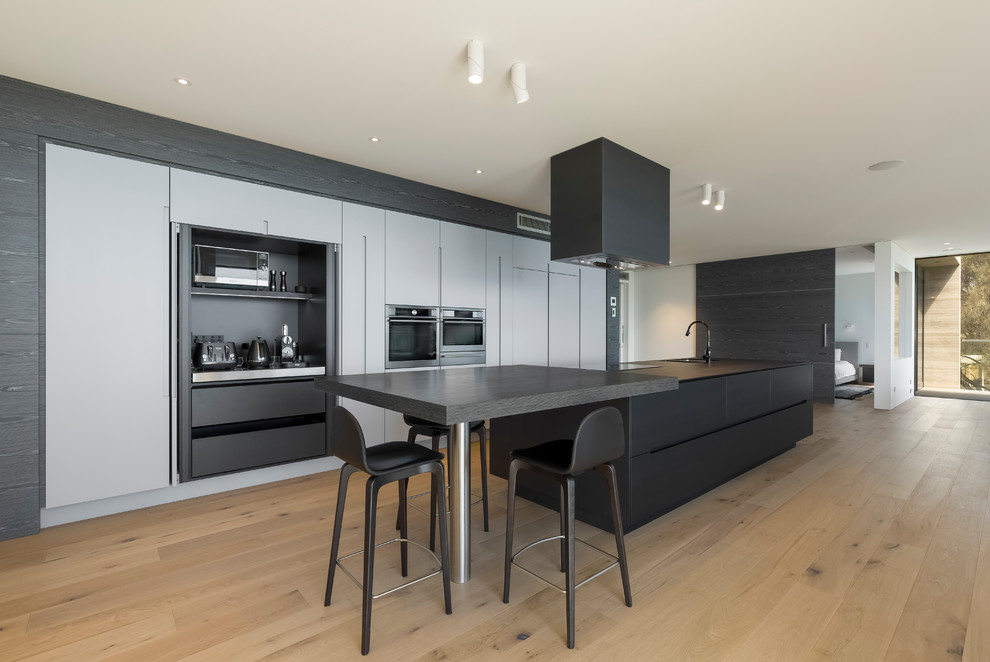 Example of a large trendy galley light wood floor open concept kitchen design in Sydney with flat-panel cabinets, dark wood cabinets, solid surface countertops, stainless steel appliances and an island