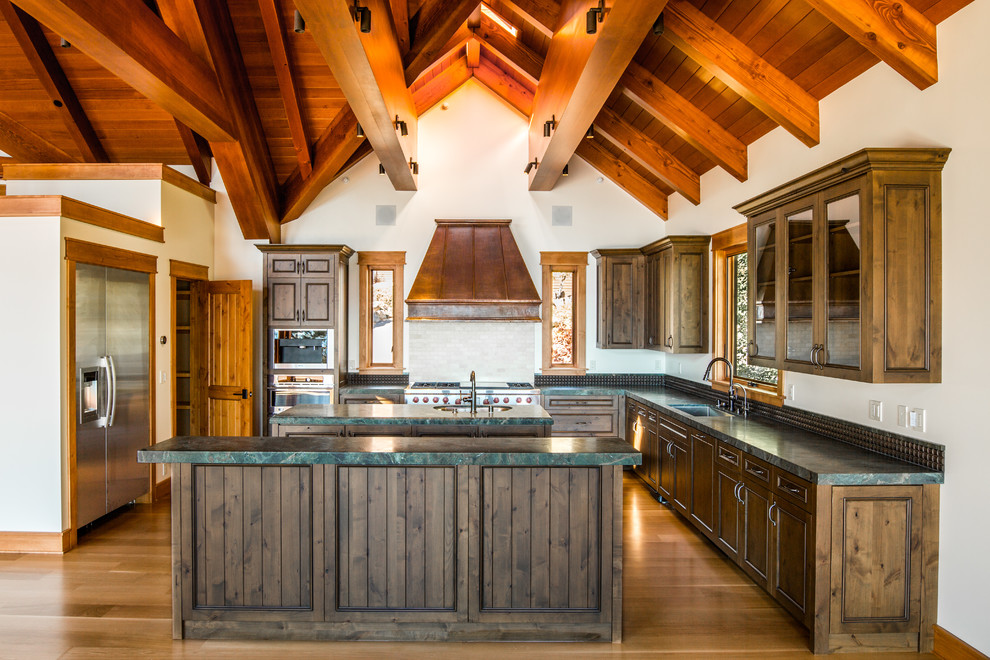 Rustik inredning av ett stort u-kök, med en undermonterad diskho, luckor med infälld panel, skåp i mellenmörkt trä, bänkskiva i täljsten, rostfria vitvaror, mellanmörkt trägolv, en köksö och brunt golv