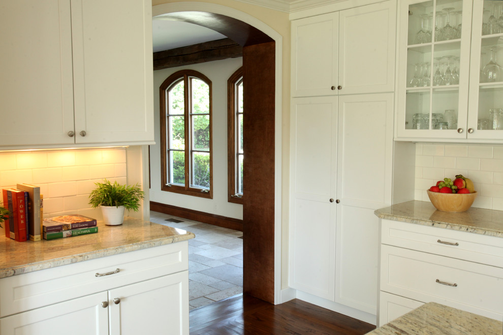 Klassisk inredning av ett mellanstort u-kök, med en undermonterad diskho, luckor med infälld panel, vita skåp, granitbänkskiva, vitt stänkskydd, stänkskydd i keramik, integrerade vitvaror, mellanmörkt trägolv och en köksö