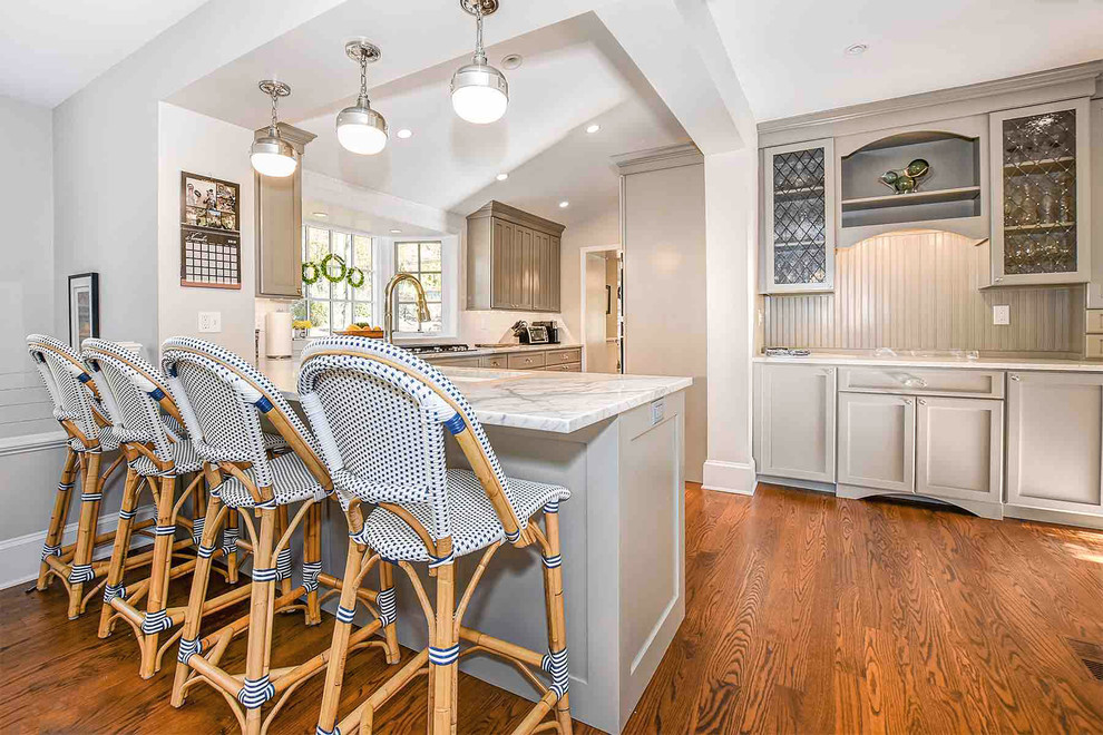 Inspiration for a mid-sized transitional l-shaped medium tone wood floor and brown floor open concept kitchen remodel in Philadelphia with a drop-in sink, shaker cabinets, gray cabinets, marble countertops, white backsplash, ceramic backsplash, stainless steel appliances, a peninsula and white countertops