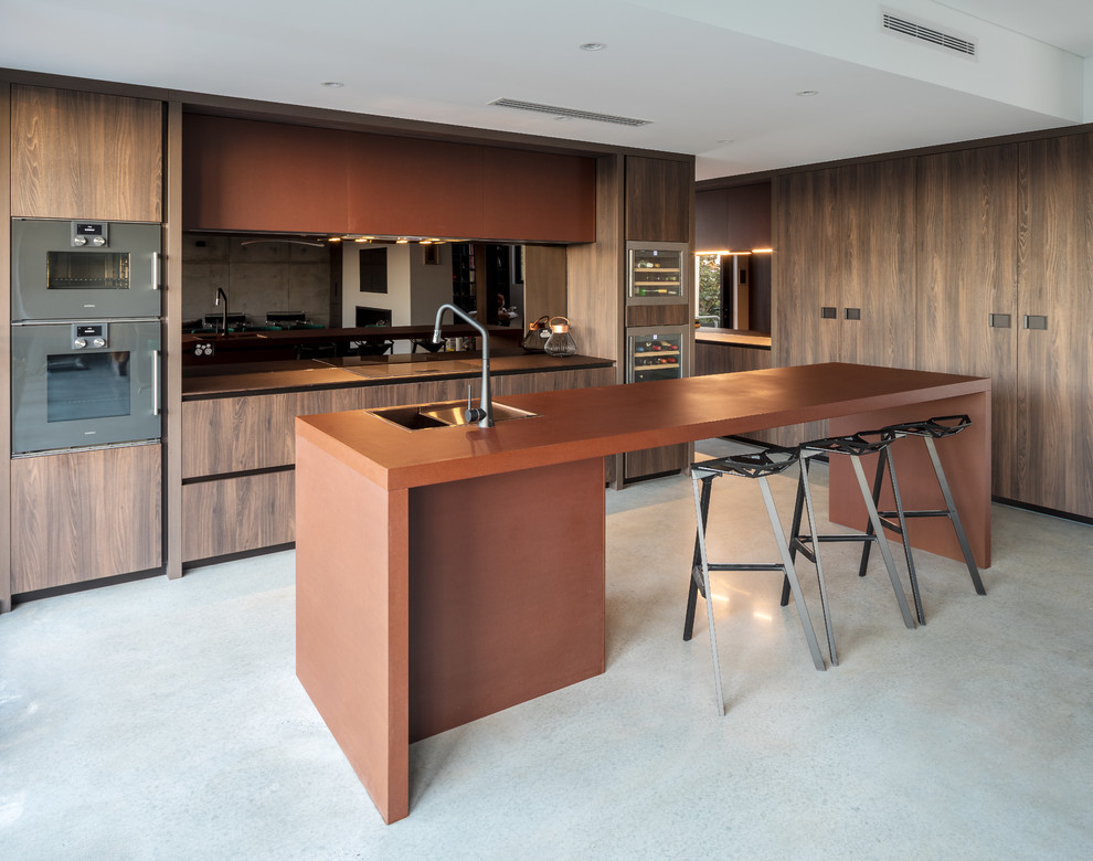 Moderne Küche in L-Form mit Unterbauwaschbecken, flächenbündigen Schrankfronten, dunklen Holzschränken, Küchengeräten aus Edelstahl, Betonboden, Kücheninsel, grauem Boden und brauner Arbeitsplatte in Perth