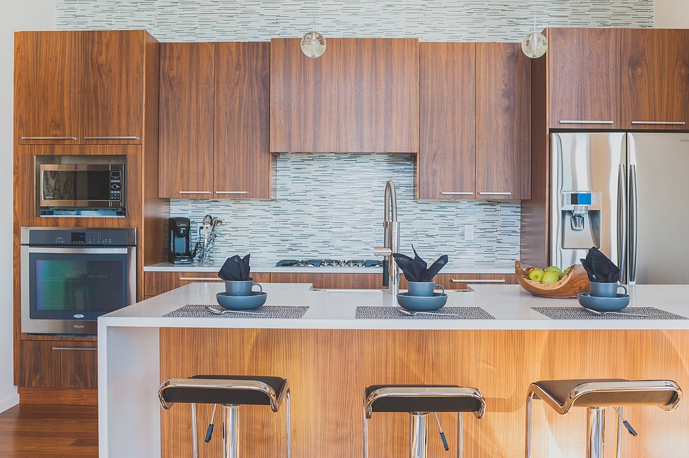 Medium sized modern galley open plan kitchen in Vancouver with a single-bowl sink, flat-panel cabinets, medium wood cabinets, engineered stone countertops, multi-coloured splashback, stainless steel appliances, bamboo flooring, an island, beige floors and brick splashback.
