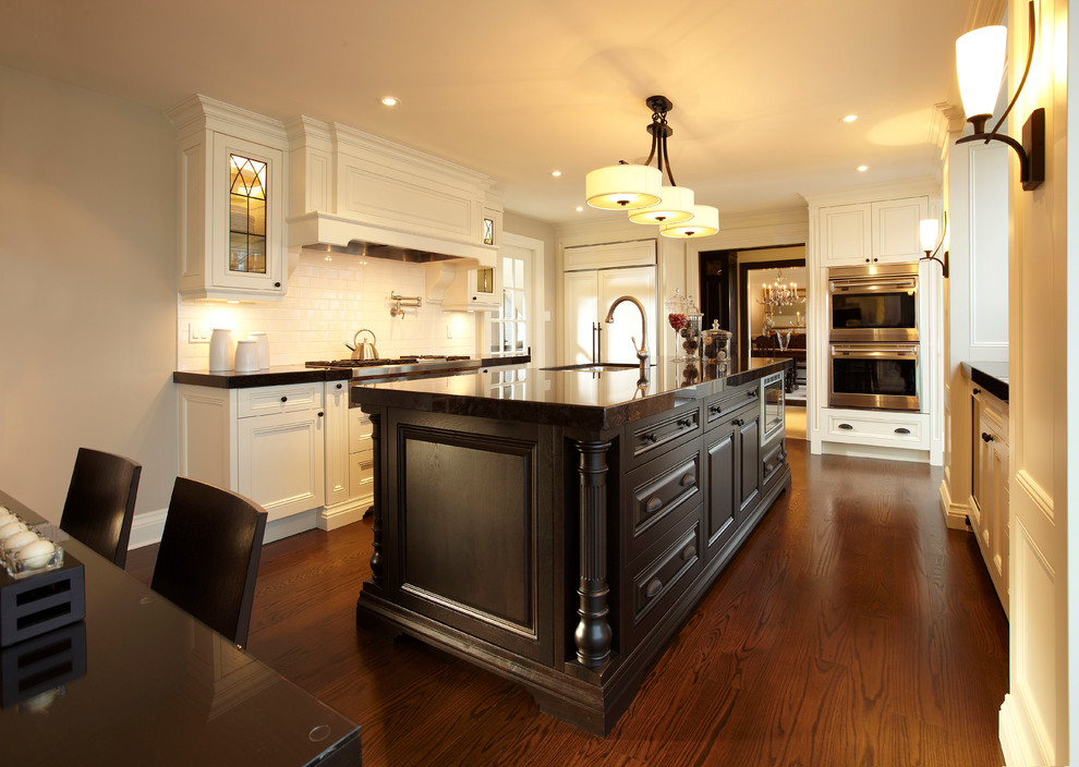 Example of a huge classic u-shaped medium tone wood floor open concept kitchen design in Toronto with an undermount sink, recessed-panel cabinets, white cabinets, granite countertops, white backsplash, subway tile backsplash, stainless steel appliances and an island