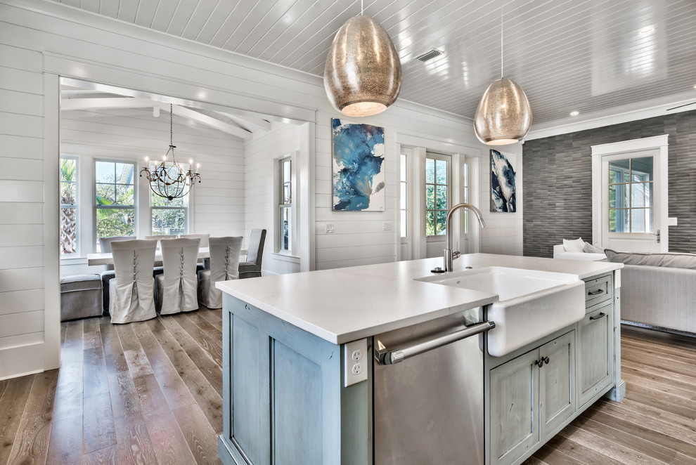 Bild på ett mellanstort maritimt vit vitt kök, med en rustik diskho, skåp i shakerstil, vita skåp, bänkskiva i kvartsit, grått stänkskydd, stänkskydd i stenkakel, rostfria vitvaror, ljust trägolv, en köksö och brunt golv