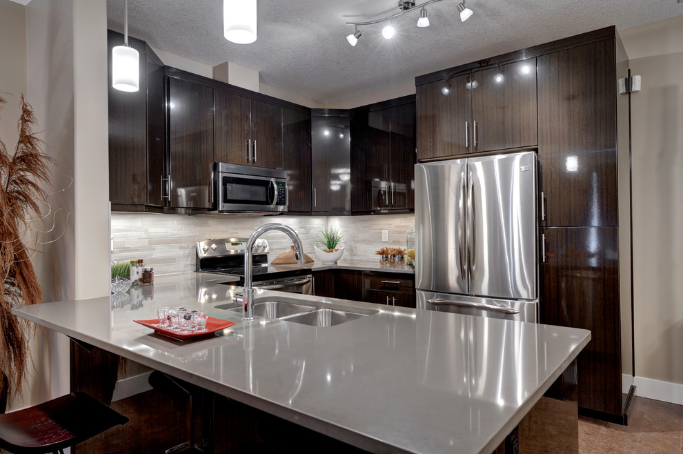 Cette image montre une cuisine américaine design en U et bois brun avec un placard à porte plane, une crédence grise et un électroménager en acier inoxydable.