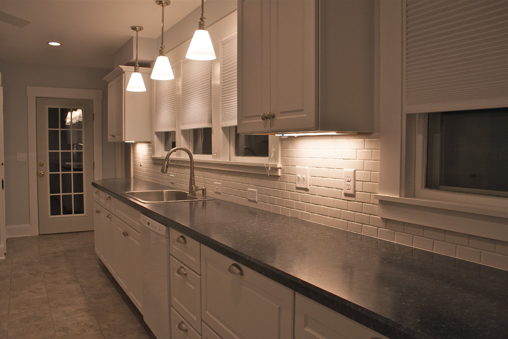 Mid-sized transitional l-shaped laminate floor kitchen photo in Boston with a double-bowl sink, raised-panel cabinets, white cabinets, solid surface countertops, white backsplash, ceramic backsplash and white appliances