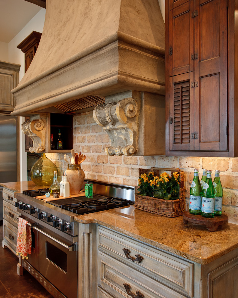Example of a large classic galley limestone floor and brown floor eat-in kitchen design in Little Rock with an undermount sink, raised-panel cabinets, distressed cabinets, granite countertops, beige backsplash, brick backsplash, stainless steel appliances and an island