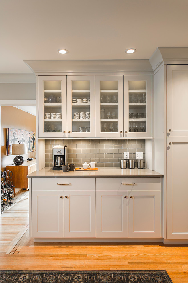 Example of a mid-sized transitional l-shaped medium tone wood floor kitchen pantry design in Vancouver with an undermount sink, recessed-panel cabinets, gray cabinets, quartz countertops, white backsplash, ceramic backsplash, stainless steel appliances and an island