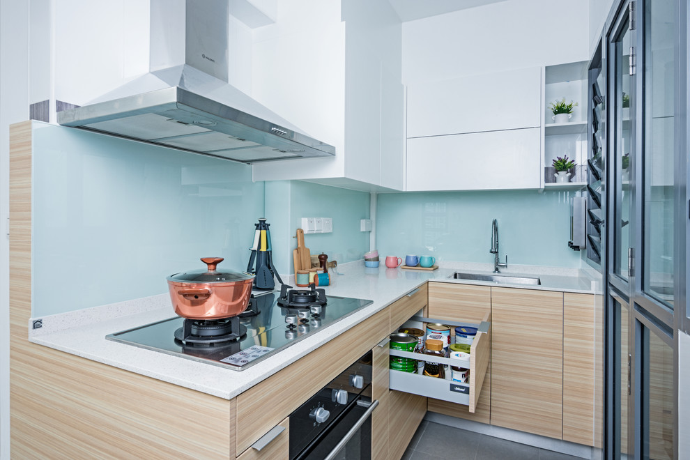 Moderne Küche in L-Form mit Unterbauwaschbecken, flächenbündigen Schrankfronten, hellen Holzschränken, Küchenrückwand in Blau, Glasrückwand, grauem Boden und weißer Arbeitsplatte in Singapur