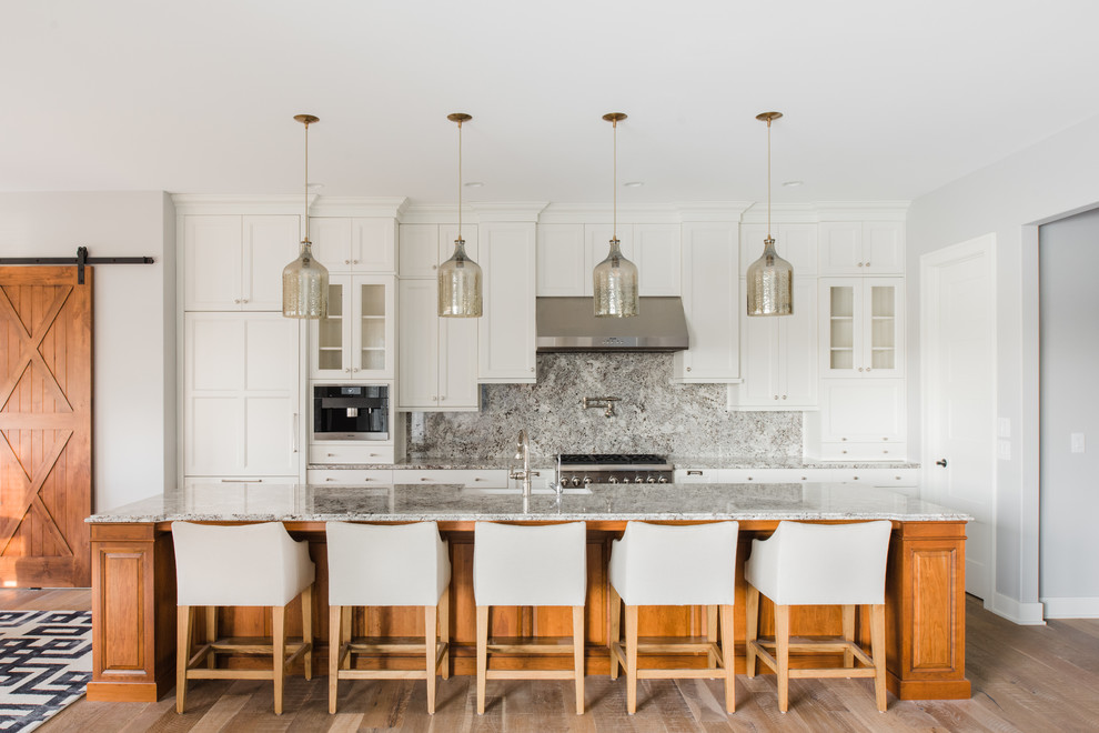Klassische Küche mit Schrankfronten im Shaker-Stil, weißen Schränken, Küchenrückwand in Grau, Küchengeräten aus Edelstahl, hellem Holzboden und Kücheninsel in Sonstige