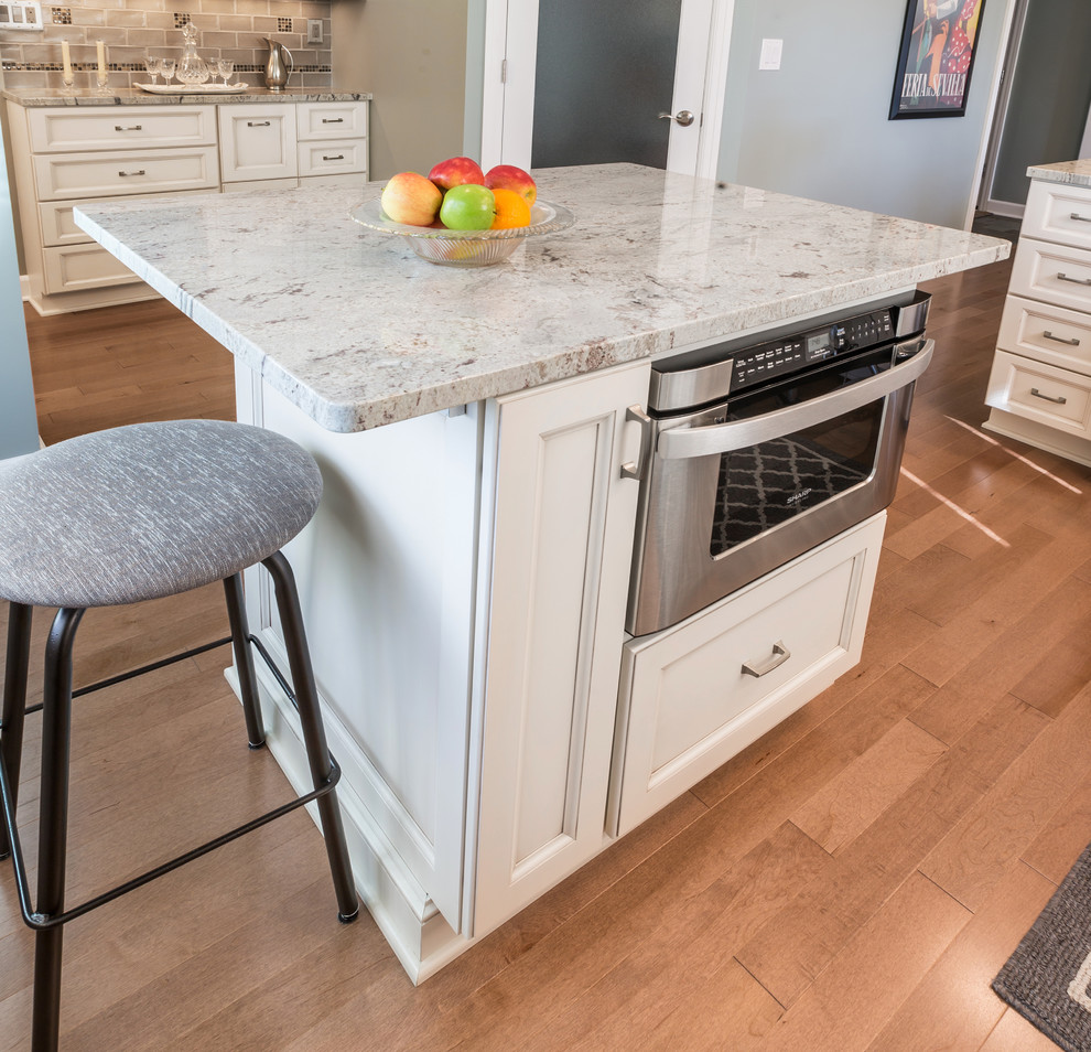 Inspiration for a mid-sized timeless u-shaped light wood floor eat-in kitchen remodel in Milwaukee with an undermount sink, recessed-panel cabinets, white cabinets, granite countertops, beige backsplash, subway tile backsplash, stainless steel appliances and an island