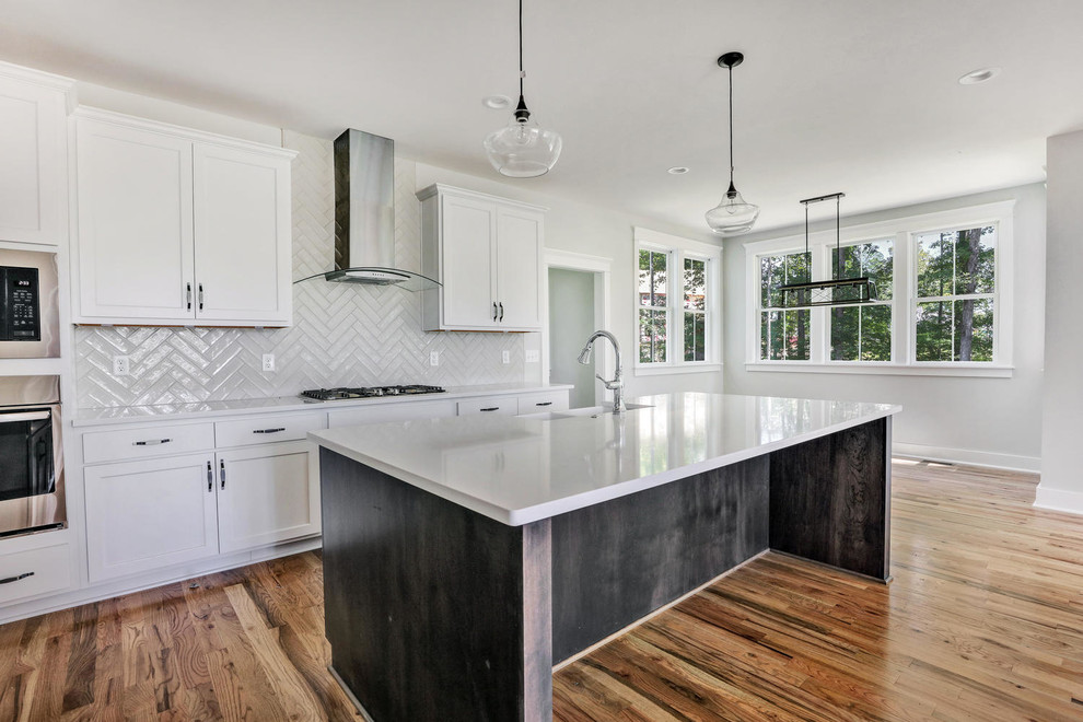 Open concept kitchen - farmhouse l-shaped light wood floor open concept kitchen idea in Richmond with a farmhouse sink, shaker cabinets, white cabinets, solid surface countertops, white backsplash, porcelain backsplash, stainless steel appliances, an island and white countertops