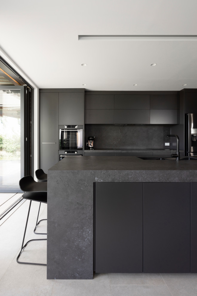 Inspiration for a medium sized contemporary galley open plan kitchen in Sydney with a submerged sink, grey floors, grey cabinets, composite countertops, grey splashback, stone slab splashback, black appliances, cement flooring, an island and grey worktops.