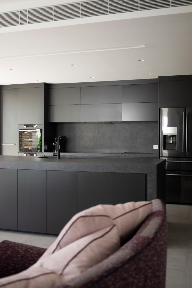 Design ideas for a medium sized contemporary galley open plan kitchen in Sydney with a submerged sink, grey cabinets, composite countertops, grey splashback, stone slab splashback, black appliances, cement flooring, an island, grey floors and grey worktops.