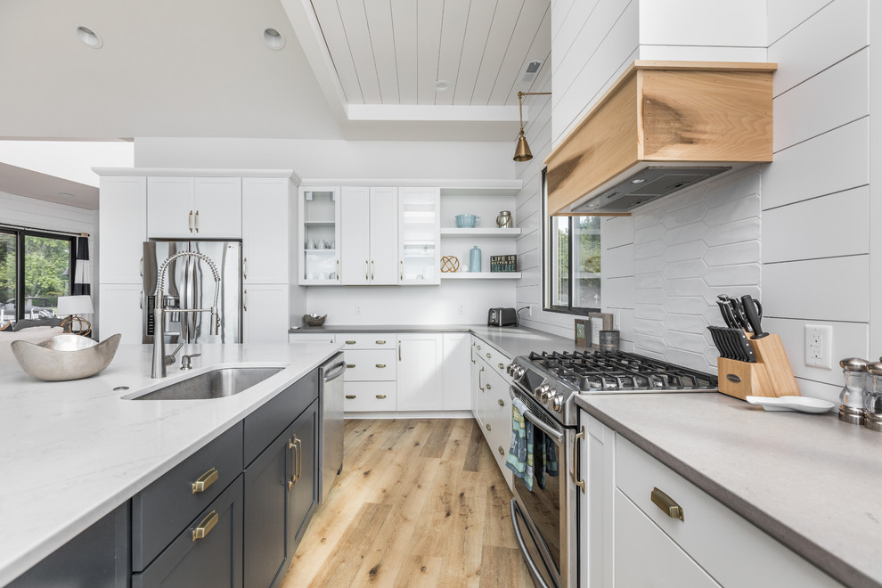 Beach style kitchen in Indianapolis with shaker cabinets, white cabinets, stainless steel appliances, light hardwood flooring, an island and grey worktops.