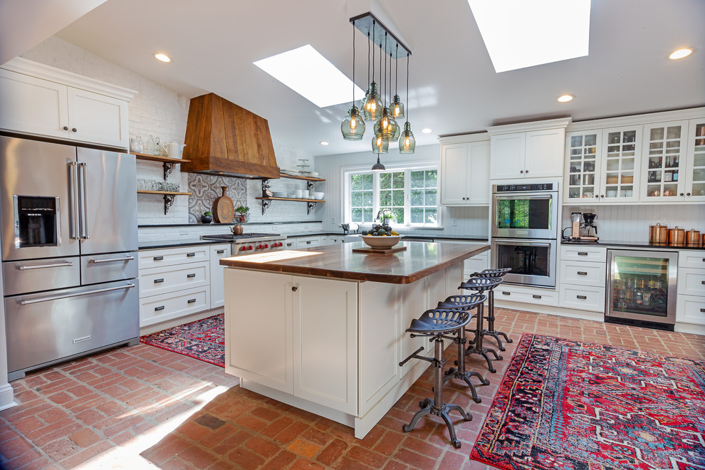 Inspiration for a farmhouse l-shaped brick floor and red floor kitchen remodel in Philadelphia with a farmhouse sink, shaker cabinets, white cabinets, white backsplash, brick backsplash, stainless steel appliances, an island and black countertops